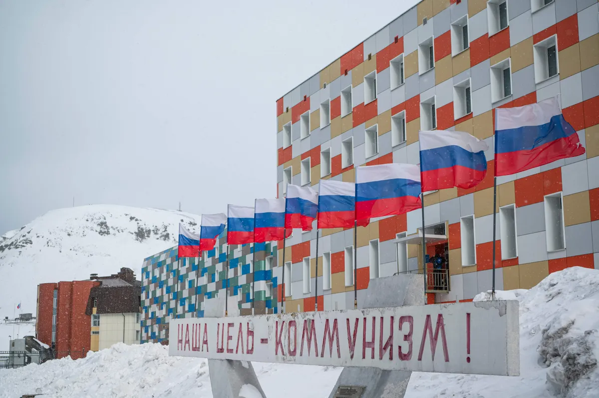 (FILES) In this file photo taken on May 07, 2022 a sign in Russian reading 'our goal is communism' is pictured in front of a building with Russian flags flapping in the blizzard, in the miners' town of Barentsburg, on the Svalbard Archipelago, northern Norway.
