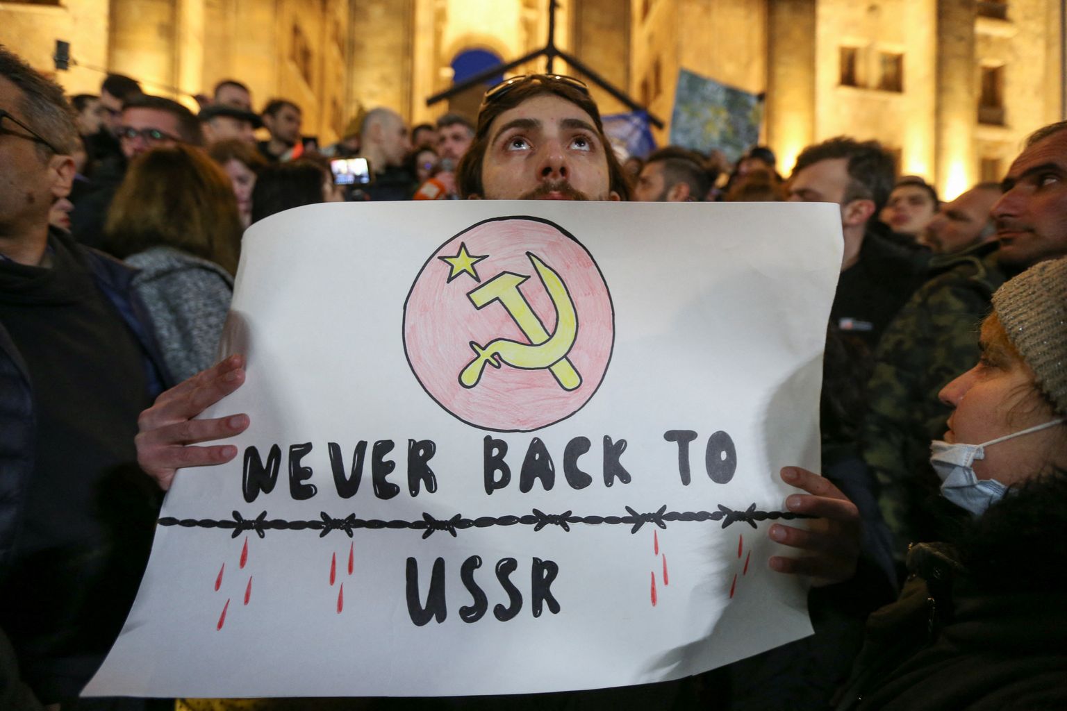 Участник акции протеста против законопроекта об «иностранных агентах», который пытаются принять грузинские власти, держит в руках плакат «Никогда не возвращаться в СССР», 8 марта 2023 года.