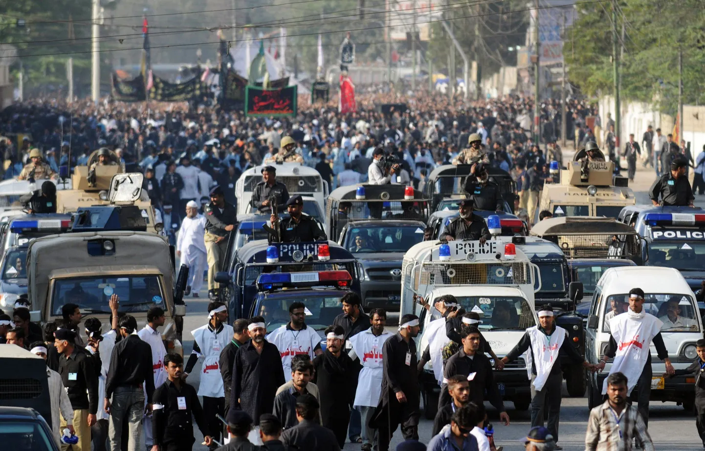 Pakistani police provides a security escort as Shiite Muslims march during a religious procession in Karachi on February 5, 2010 to mark the 40th day of mourning after the anniversary of the death of Imam Hussain, the grandson of the Prophet Mohammed. Two suicide bombers on motorcycles struck a bus and hospital in Karachi on February 5, killing 23 people and targeting Shiite Muslims in Pakistan's financial capital for the second time in six weeks. Women and children were among 12 people killed when a bomber rammed a motorcycle bomb into a bus of Shiites on one of Karachi's busiest roads, gutting the bus and sending glass flying, officials and witnesses said.  A second bomber killed 11 people, damaging ambulances and the entrance to the casualty department at Jinnah Hospital where the bomb victims were being treated and anxious relatives were gathering. AFP PHOTO/ RIZWAN TABASSUM